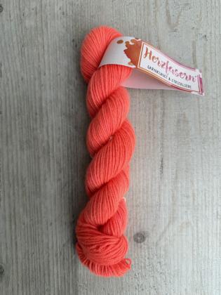 Strang aus 100 Prozent Kaschmir in leuchtendem Koralle-Neon mit Banderole Herzfasern auf hellem Holzuntergrund fotografiert.